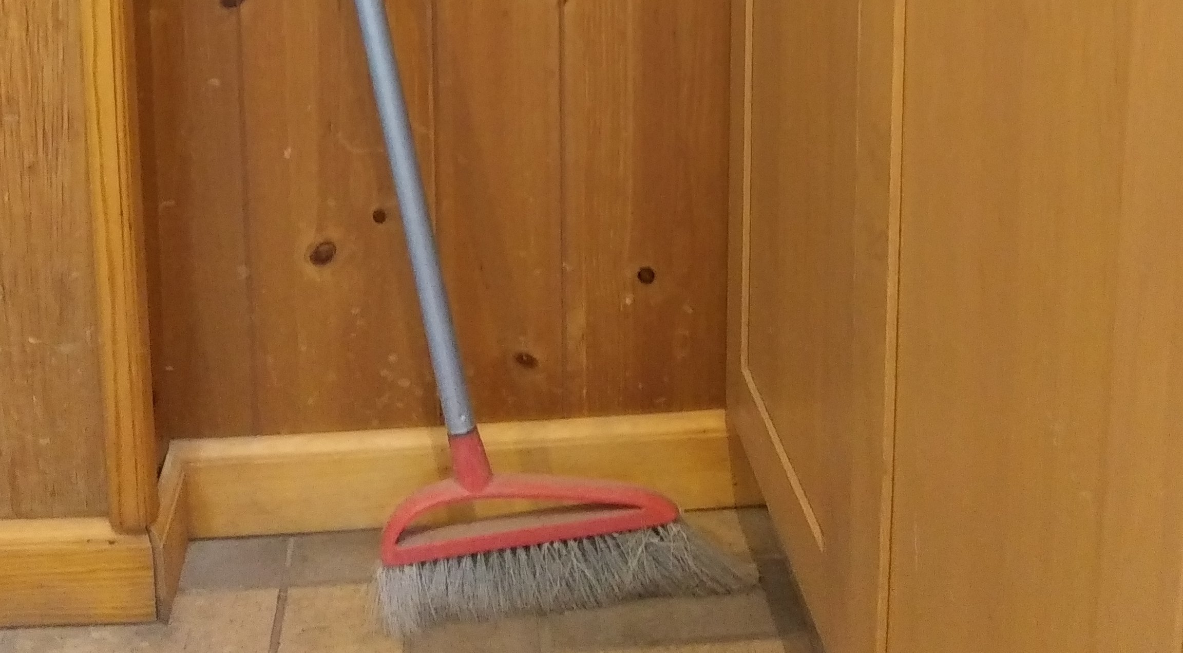 Broom leaning against paneled wall.